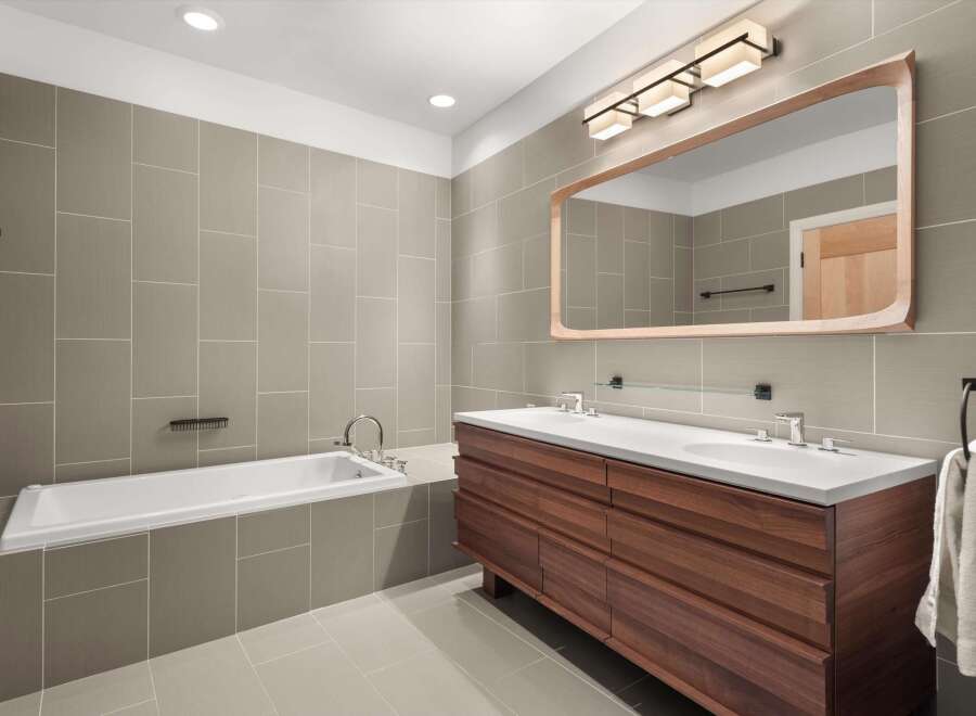 This modern bathroom features a sleek design with a large wooden vanity and a matching mirror frame.