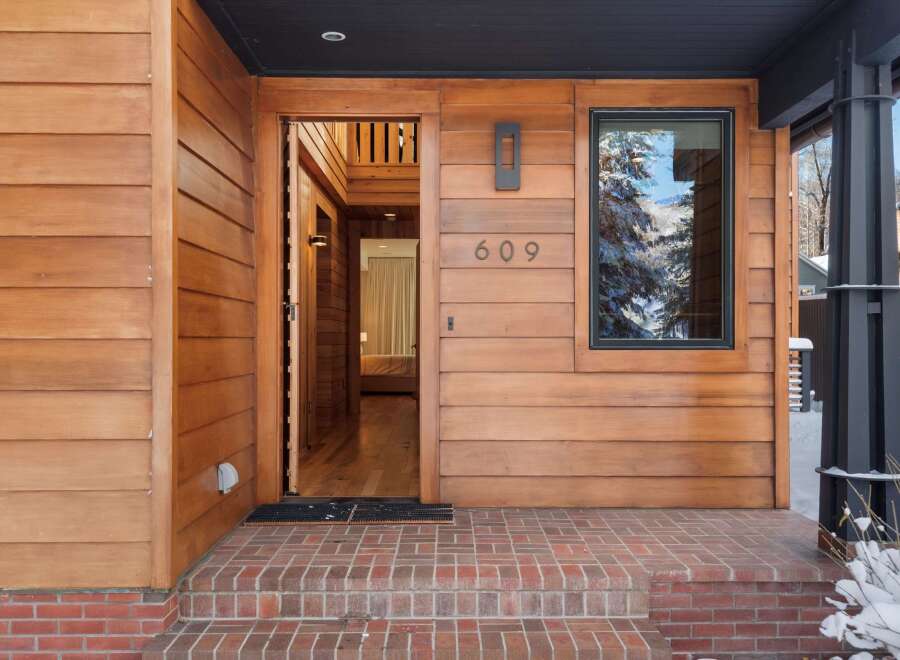 This stunning property features a welcoming entrance with a wooden facade and a modern design.