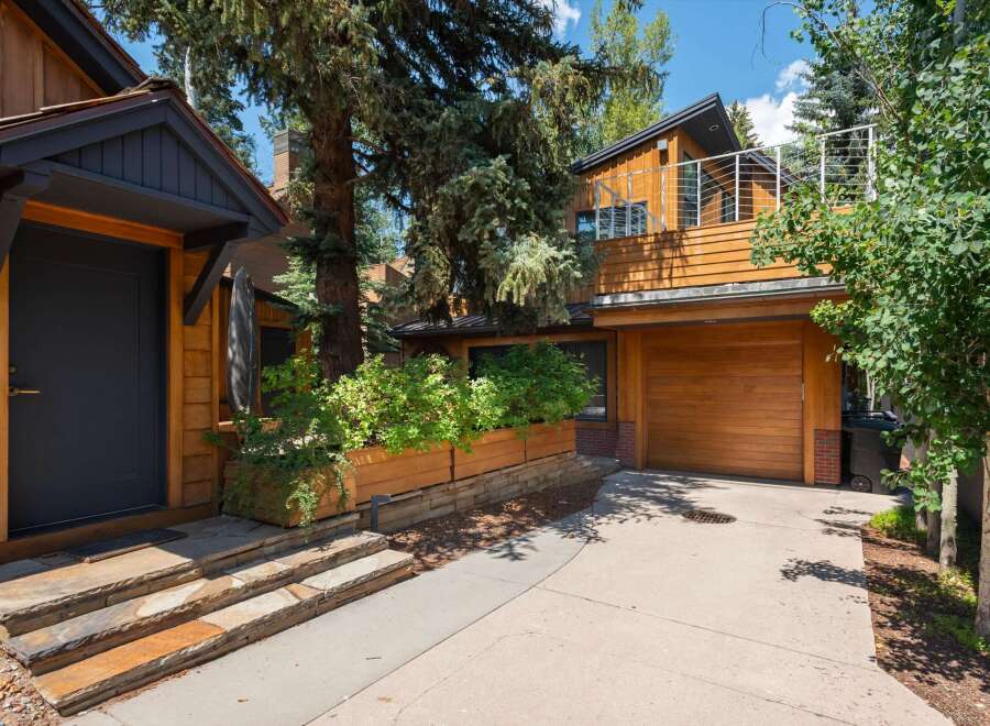 Experience modern mountain living in this stunning home featuring a sleek dark entryway with natural wood siding and stone steps.