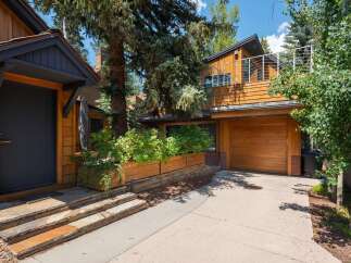 Experience modern mountain living in this stunning home featuring a sleek dark entryway with natural wood siding and stone steps.