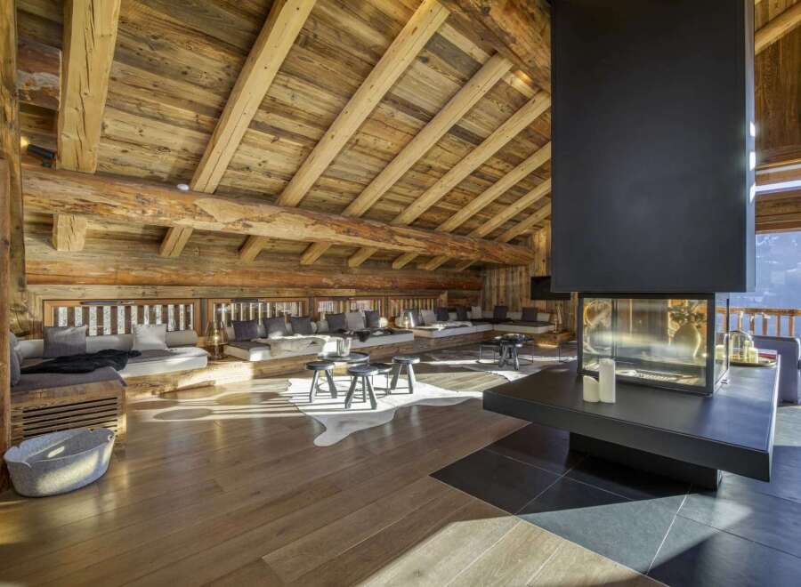 Experience luxury living in this stunning chalet, featuring a cozy living area with a fireplace and wooden beams.