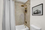 Step into a beautifully designed bathroom featuring a modern shower with a stylish gold showerhead and a sleek white bathtub.
