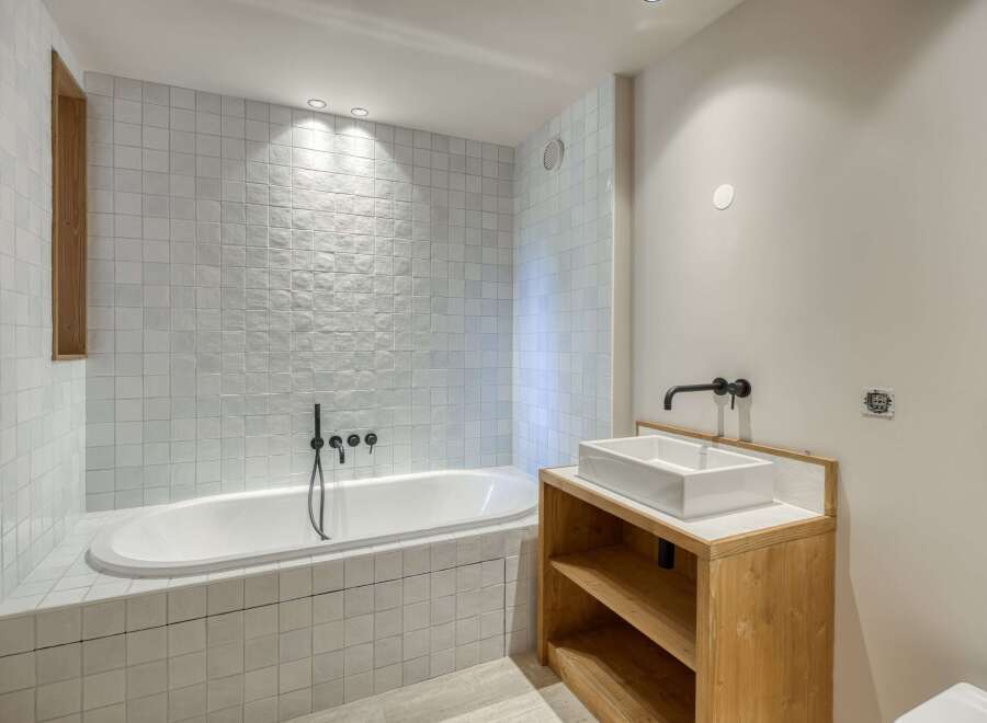 This modern bathroom features a sleek design with a white bathtub and matching square tiles.