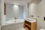 This modern bathroom features a sleek design with a white bathtub and matching square tiles.