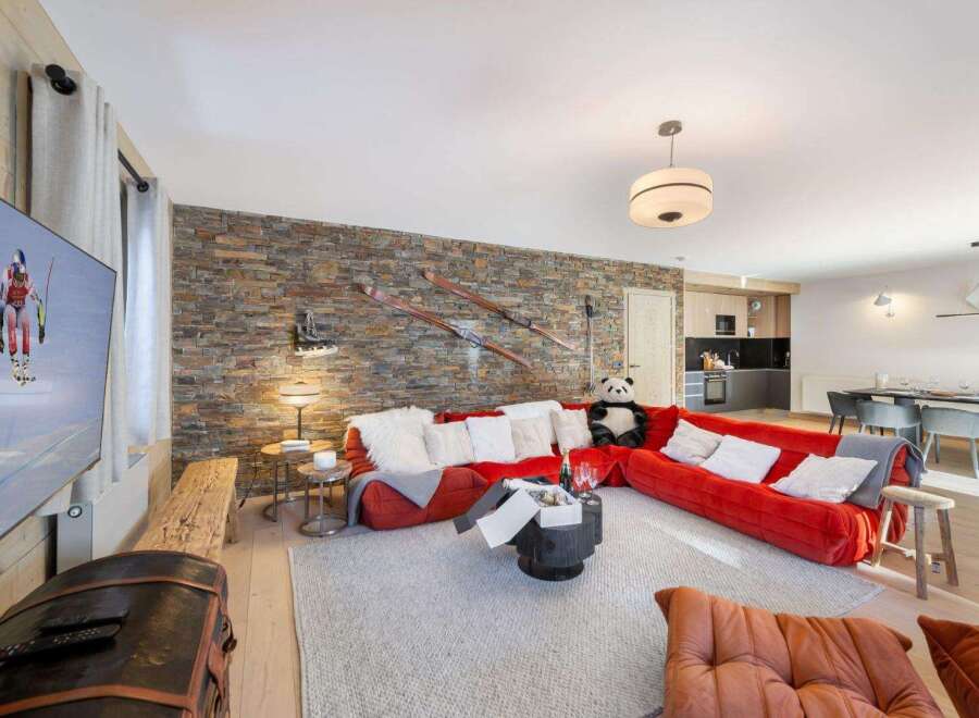 Experience luxury living in this stunning property, featuring a cozy living room with a striking stone wall and a vibrant red sofa.