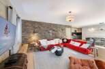 Experience luxury living in this stunning property, featuring a cozy living room with a striking stone wall and a vibrant red sofa.