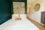This cozy bedroom features a stylish design with a dark teal accent wall that complements the light wooden bed frame.