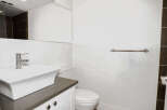This modern bathroom features a sleek white sink and vanity, complemented by a stylish chrome faucet and towel rack.