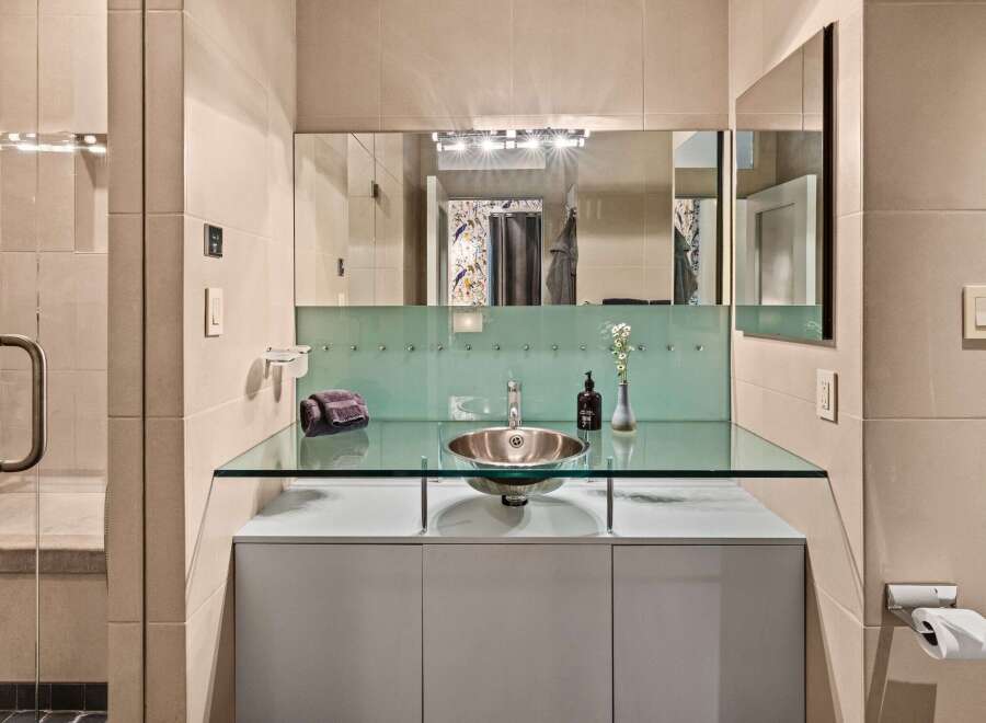 This modern bathroom showcases a sleek design with a glass countertop and a stylish vessel sink.