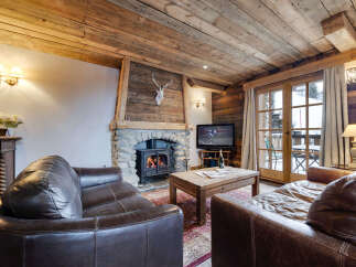 Experience the warmth of this charming chalet, featuring a cozy living room with a stone fireplace and exposed wooden beams.