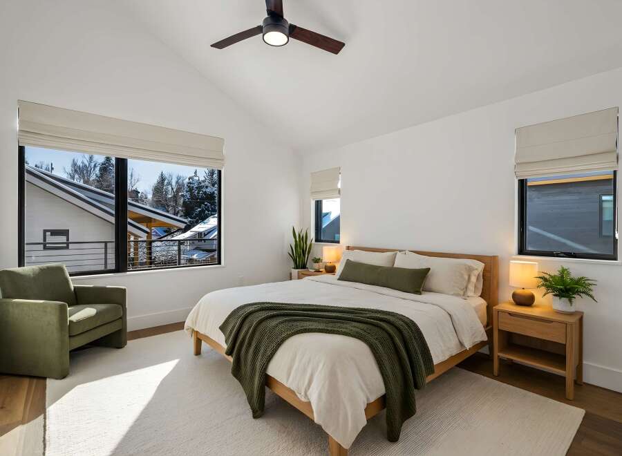 Experience modern comfort in this serene bedroom, featuring a vaulted ceiling with a stylish fan and expansive windows that offer picturesque winter views.