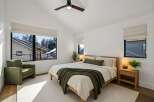 Experience modern comfort in this serene bedroom, featuring a vaulted ceiling with a stylish fan and expansive windows that offer picturesque winter views.