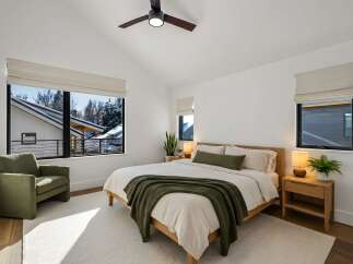 Experience modern comfort in this serene bedroom, featuring a vaulted ceiling with a stylish fan and expansive windows that offer picturesque winter views.