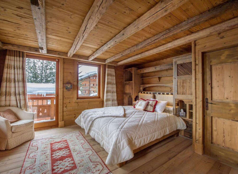 Experience the rustic charm of this cozy bedroom, featuring warm wooden walls and a beamed ceiling.