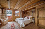 Experience the rustic charm of this cozy bedroom, featuring warm wooden walls and a beamed ceiling.