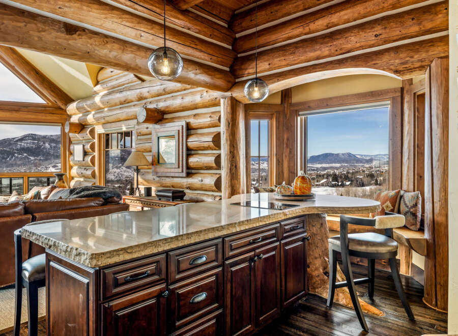 Experience the rustic charm of this stunning log cabin kitchen, featuring a beautiful island with a granite countertop and dark wood cabinetry.