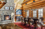 This stunning dining room showcases rustic elegance with its log cabin architecture and stone fireplace.