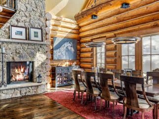 This stunning dining room showcases rustic elegance with its log cabin architecture and stone fireplace.