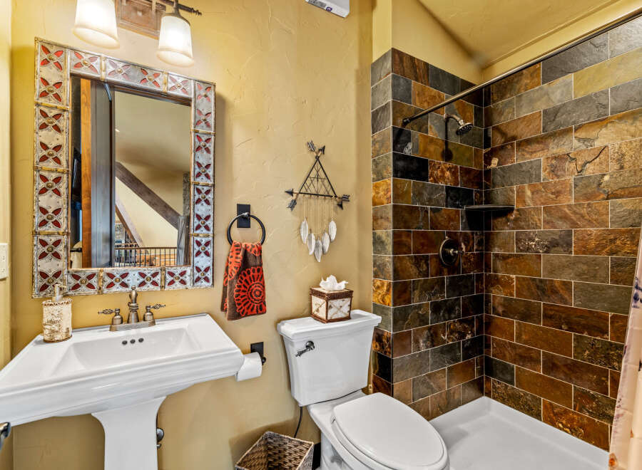 This stunning bathroom boasts a rustic charm with its stone-tiled shower and decorative mirror.