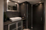 Experience modern luxury in this sleek bathroom featuring a spacious walk-in shower with dark tiled walls and a rainfall showerhead.
