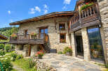 Experience rustic charm in this stone mountain home, featuring wooden balconies adorned with vibrant flowers and expansive windows offering breathtaking views.