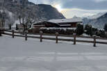 Nestled in a serene winter landscape, this charming property boasts a cozy wooden house with a snow-covered roof.