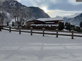 Nestled in a serene winter landscape, this charming property boasts a cozy wooden house with a snow-covered roof.