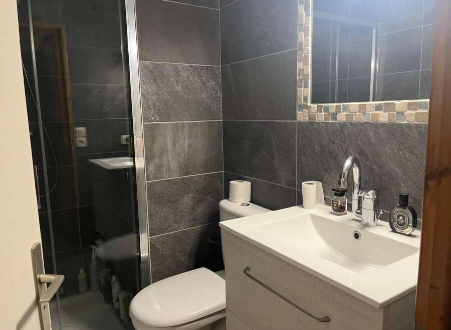 This modern bathroom features sleek, dark gray tiles and a glass shower enclosure, creating a sophisticated and contemporary feel.