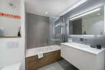 This modern bathroom features a sleek design with gray tiled walls and a wooden accent on the bathtub.