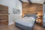 This stunning bedroom boasts a rustic charm with its wooden accent wall and exposed beams, creating a warm and inviting atmosphere.