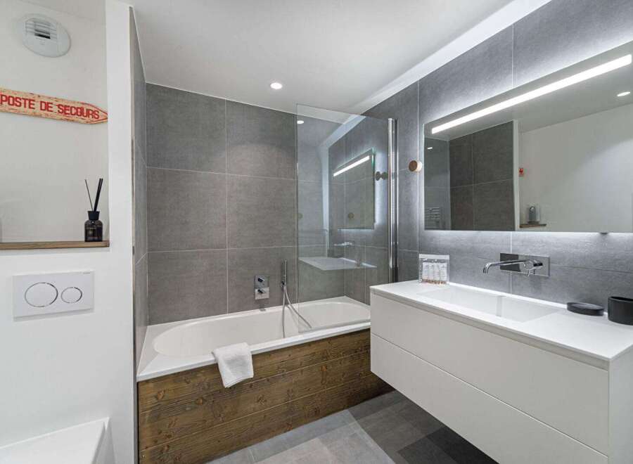 This modern bathroom features a sleek design with gray tiled walls and a wooden accent on the bathtub.
