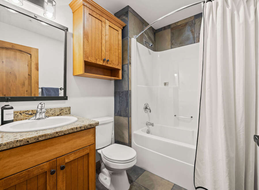 This stunning bathroom features a beautiful wooden vanity with a granite countertop, offering both style and functionality.