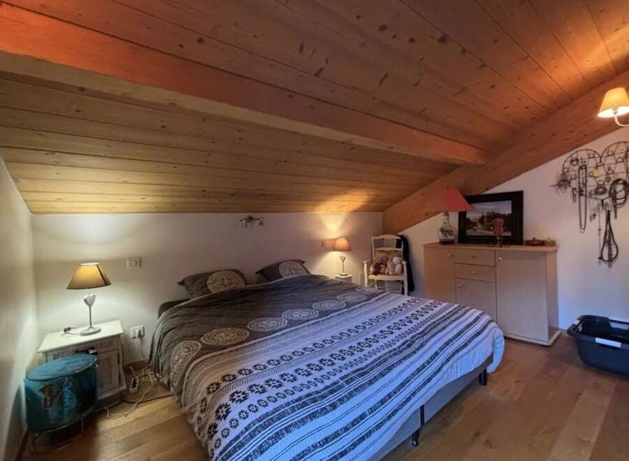 This cozy bedroom features a unique sloped ceiling with exposed wooden beams, creating a warm and inviting atmosphere.