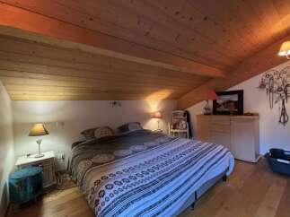 This cozy bedroom features a unique sloped ceiling with exposed wooden beams, creating a warm and inviting atmosphere.