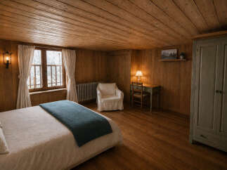 Experience rustic charm in this cozy bedroom, featuring warm wooden walls and ceiling, a comfortable bed with a teal throw, and a vintage-inspired desk with a lamp.