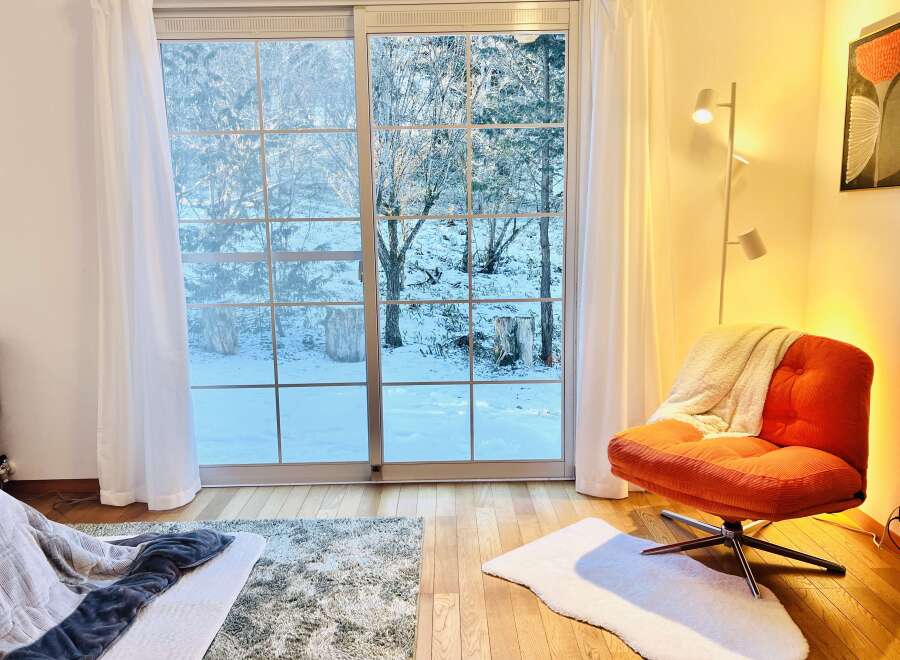 Enjoy the serene beauty of this cozy living space, featuring a stunning view of a snow-covered landscape through large sliding glass doors.