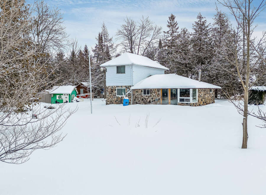 This stunning property features a charming two-story house with a unique stone facade, perfect for a cozy winter retreat.