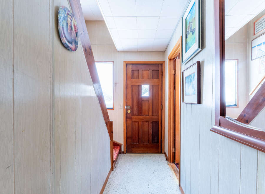 Step into this inviting entryway, featuring a warm wooden door and a charming staircase.