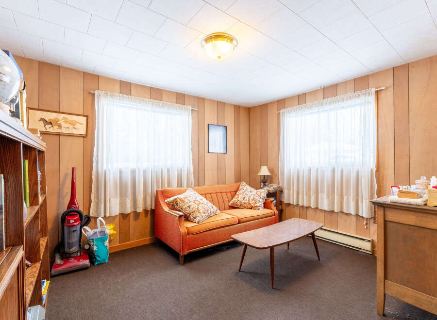 Step into this cozy living space, featuring warm wood paneling and ample natural light from the large windows.