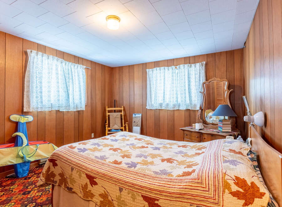Step into this cozy bedroom featuring warm wood paneling and a charming ambiance.