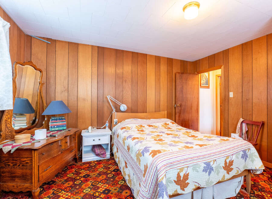 Step into this cozy bedroom featuring warm wood paneling and a charming vintage aesthetic.