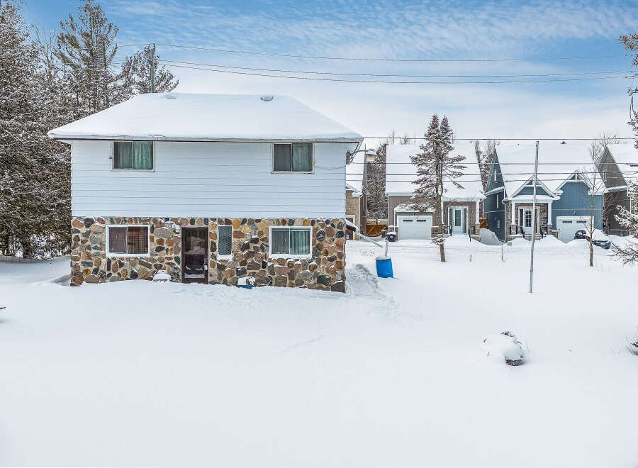 This charming property features a unique stone facade and a snow-covered roof, creating a cozy winter scene.