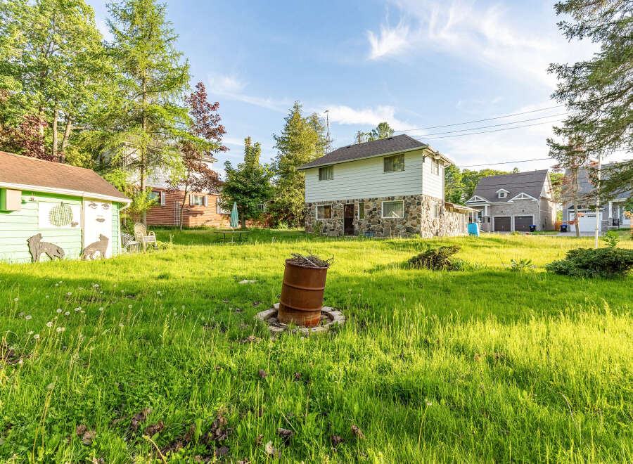 Discover this charming property featuring a unique two-story home with a stone foundation and siding, complemented by a detached green shed adorned with whimsical wolf cutouts.
