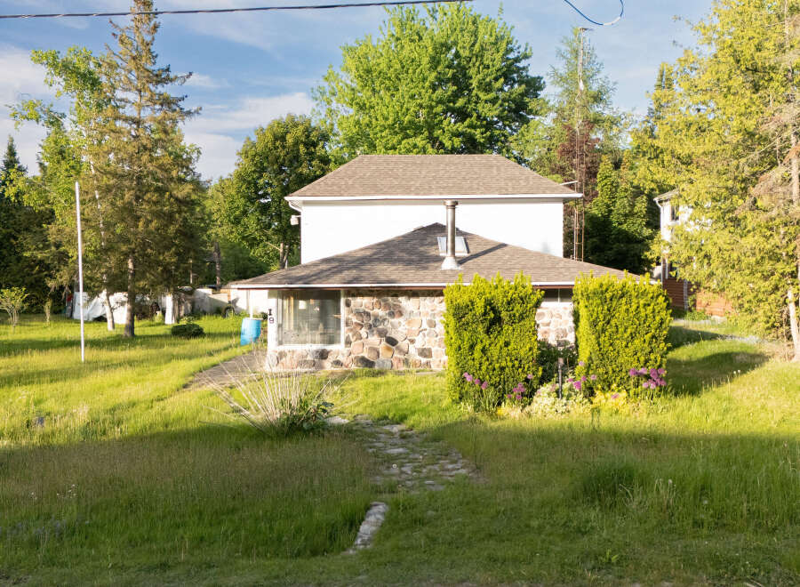 Discover this charming home featuring a unique stone facade on the lower level, complemented by lush green landscaping and mature trees.