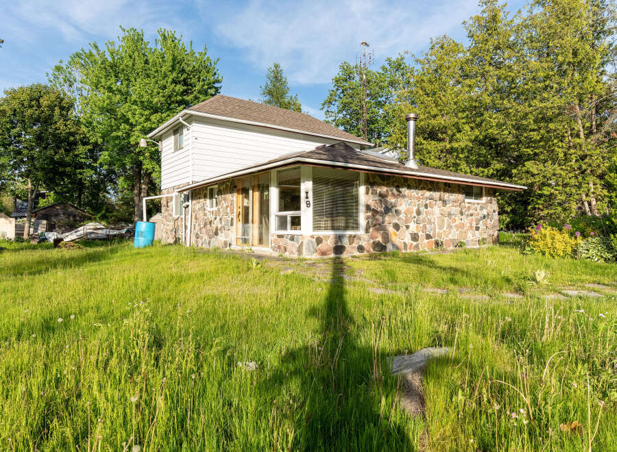 Charming property featuring a unique stone-clad lower level and a white-sided upper story, set amidst lush green grass and mature trees.