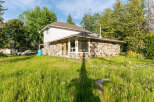 Charming property featuring a unique stone-clad lower level and a white-sided upper story, set amidst lush green grass and mature trees.