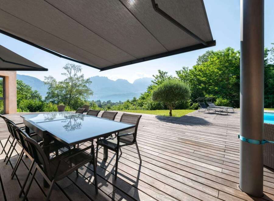 Enjoy outdoor living at its finest with this stunning property featuring a spacious wooden deck and a modern glass-top dining table, perfect for entertaining.