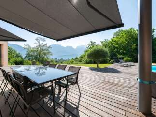 Enjoy outdoor living at its finest with this stunning property featuring a spacious wooden deck and a modern glass-top dining table, perfect for entertaining.