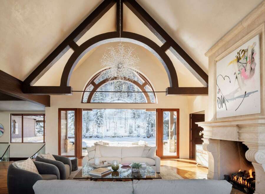 Experience luxury living in this stunning property, featuring a spacious living room with a grand fireplace and a breathtaking view of the snowy landscape.