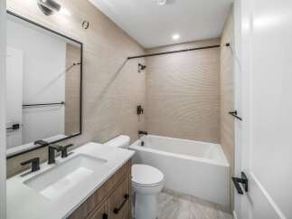 Step into a modern bathroom oasis! This space features a sleek vanity with a pristine white countertop, complemented by a stylish mirror and contemporary fixtures.